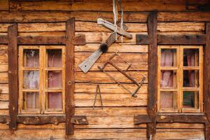 An old wooden wall of a house with windows in the village and tools hanging photo