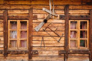 An old wooden wall of a house with windows in the village and tools hanging photo