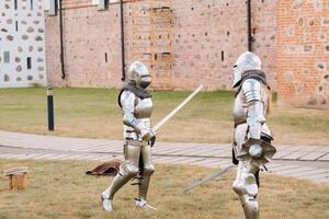 two knights in ancient metal armor are standing at the stone wall of the castle fighting with swords photo
