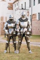 two knights in ancient metal armor stand at the stone wall of the castle photo