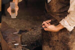 A blacksmith manually forges red-hot metal on an anvil with a hammer photo