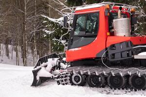 A snowplow on red tracks standing in winter in the forest near the barn photo