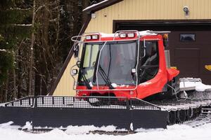 A snowplow on red tracks standing in winter in the forest near the barn photo