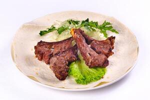 Meat kebab on ribs on lavash with onions and cabbage on a white plate, on an isolated white background photo
