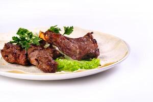 Meat kebab on ribs on lavash with onions and cabbage on a white plate, on an isolated white background photo