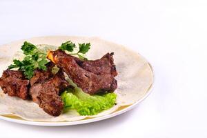 Meat kebab on ribs on lavash with onions and cabbage on a white plate, on an isolated white background photo