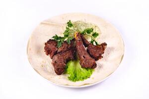 Meat kebab on ribs on lavash with onions and cabbage on a white plate, on an isolated white background photo