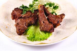 Meat kebab on ribs on lavash with onions and cabbage on a white plate, on an isolated white background photo