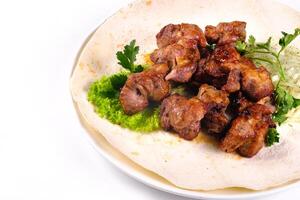 Pork shish kebab on lavash lies in a white plate on a white isolated background photo