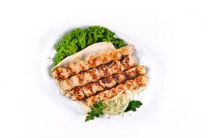 Homemade kebab on skewers with pita bread, onions, cabbage, vegetables, on a white plate on an isolated white background photo