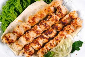 Homemade kebab on skewers with pita bread, onions, cabbage, vegetables, on a white plate on an isolated white background photo