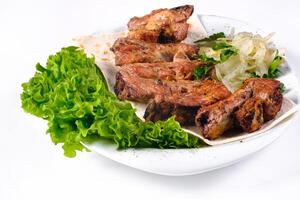 Meat kebab on ribs on lavash with onions and cabbage on a white plate, on an isolated white background photo