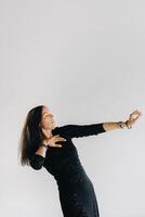 A girl in a black dress moves in a dance on a gray background. Dynamic dance photo