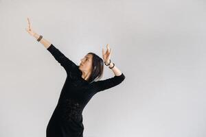 A girl in a black dress moves in a dance on a gray background. Dynamic dance photo