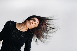 A girl in a black dress moves in a dance on a gray background. Dynamic dance photo