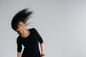 A girl in a black dress moves in a dance on a gray background. Dynamic dance photo