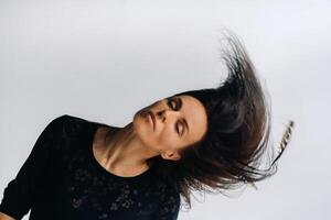 A girl in a black dress moves in a dance on a gray background. Dynamic dance photo