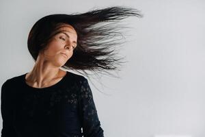 A girl in a black dress moves in a dance on a gray background. Dynamic dance photo