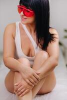 a slender woman is sitting on a bed in a beauty salon before laser hair removal. look at the delicate skin on your legs and want to make it more hairless photo