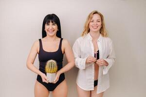 Cactus concept. Unshaven body . One girl is holding a cactus in her hands, and the second girl is holding a razor. Symbol of unshaven body parts photo