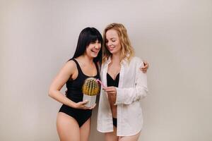 Cactus concept. Unshaven body . One girl is holding a cactus in her hands, and the second girl is holding a razor. Symbol of unshaven body parts photo