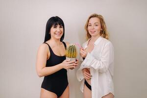 Cactus concept. Unshaven body . One girl is holding a cactus in her hands, and the second girl is holding a razor. Symbol of unshaven body parts photo