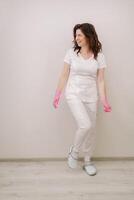 A smiling doctor in pink gloves and a white coat looks at the camera on a light background photo