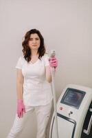 Portrait of the master of laser hair removal. A woman in a white coat holds a laser hair removal device in her hands photo