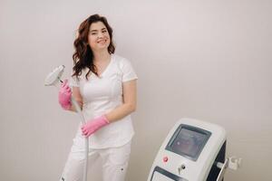 Portrait of the master of laser hair removal. A woman in a white coat holds a laser hair removal device in her hands photo