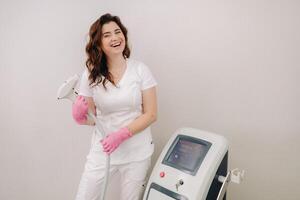 Portrait of the master of laser hair removal. A woman in a white coat holds a laser hair removal device in her hands photo
