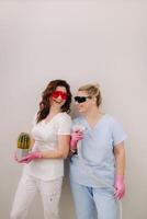 Two cosmetologists in protective glasses are holding a laser depilation device and a cactus in their hands photo
