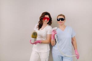 Two cosmetologists in protective glasses are holding a laser depilation device and a cactus in their hands photo