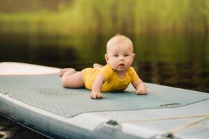 The child lies floating on the water on a large sup board. Water sports photo