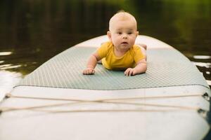 The child lies floating on the water on a large sup board. Water sports photo