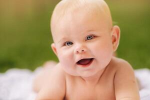 Cute happy toddler lying on a blanket on the grass outdoors in summer photo
