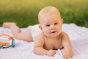 Cute happy toddler lying on a blanket on the grass outdoors in summer photo