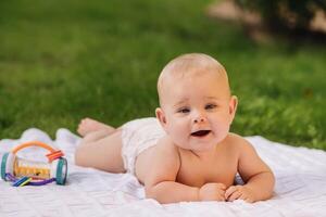 Cute happy toddler lying on a blanket on the grass outdoors in summer photo