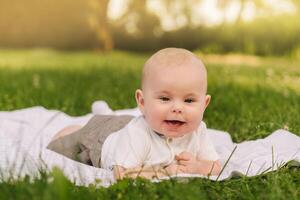 Cute happy toddler lying on a blanket on the grass outdoors in summer photo