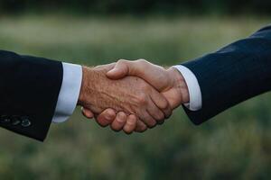 Two business people shaking hands in front of a field photo