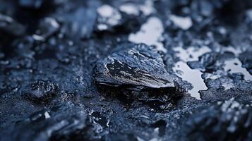Rock with a dark blue hue is on a wet surface. The rock is surrounded by other rocks and he is the only one with a different color. The wet surface gives the image a moody and mysterious feel photo