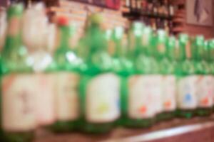 Blurred image of Soju or Korean burned liquor in green glass bottles on the countertop at the pub or restaurant for background. photo