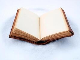 An open book lies on a bed of snow, creating a striking contrast between the warm, aged pages and the cold, white snow. photo