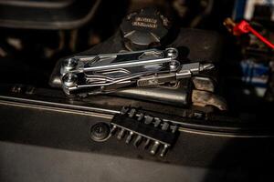 A multi-tool with various attachments is placed on a car engine, highlighting its utility for automotive repairs, with a set of interchangeable bits nearby photo