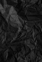 A sheet of black wrinkled paper. Texture of black crumpled paper. Dark paper background with chaotic bends. photo