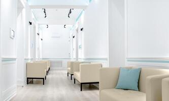 Modern waiting room with beige armchairs, light blue accents, and white walls, clean and minimalistic design, bright lighting, comfortable seating, suitable for medical or professional offices. photo