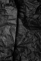 A sheet of black wrinkled paper. Texture of black crumpled paper. Dark paper background with chaotic bends. photo