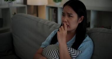 Handheld high angle view shot, Young Asian woman watching an exciting movie with a shocked and thrilled expression while sitting on a sofa in her living room at home. Leisure activity. video