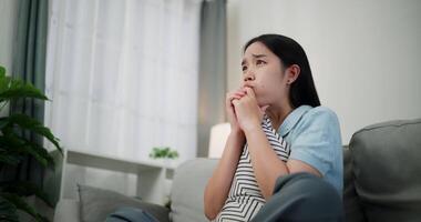 Handheld low angle view shot, An attractive young woman is intently watching something on TV and shows signs of extreme excitement and joy while sitting on sofa in the living room at home. video