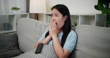 Handheld shot, Young Asian woman watching an exciting movie with a shocked and thrilled expression while sitting on a sofa in her living room at home. Leisure activity, Lifestyle concept. video