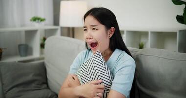 Handheld high angle view shot, An attractive young woman is intently watching something on TV and shows signs of extreme excitement and joy while sitting on sofa in the living room at home. video
